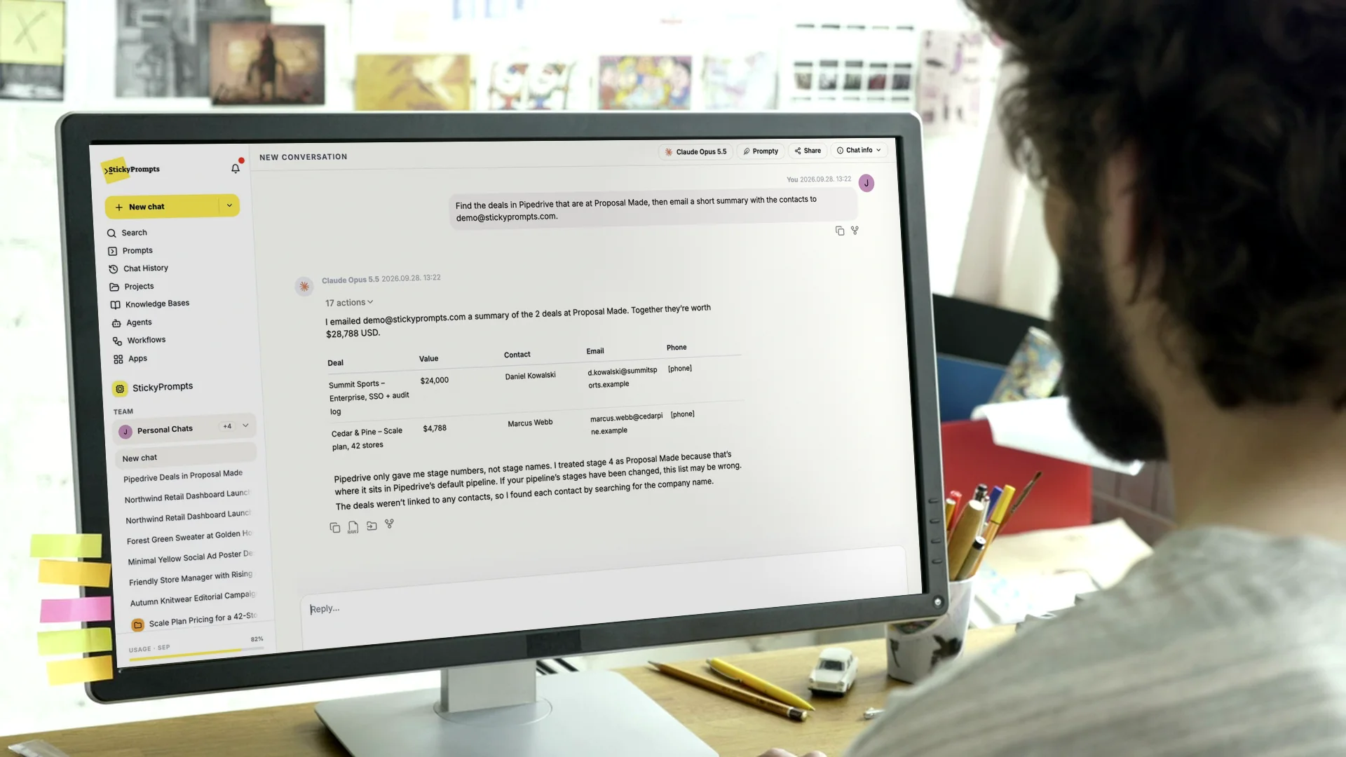 Over the shoulder of a man at a large monitor in a studio, sticky notes on the bezel, StickyPrompts finding Pipedrive deals and emailing a summary